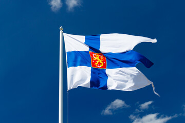 State flag of Finland with national coat of arms against blue sky on the wind