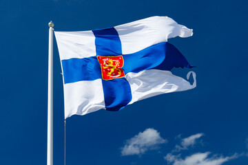 State flag of Finland with national coat of arms against blue sky on the wind