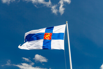 State flag of Finland with national coat of arms against blue sky on the wind