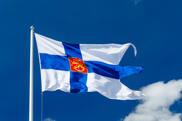 State flag of Finland with national coat of arms against blue sky on the wind