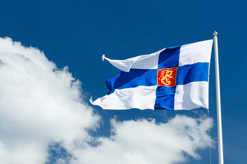 State flag of Finland with national coat of arms against blue sky on the wind