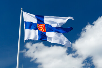 State flag of Finland with national coat of arms against blue sky on the wind