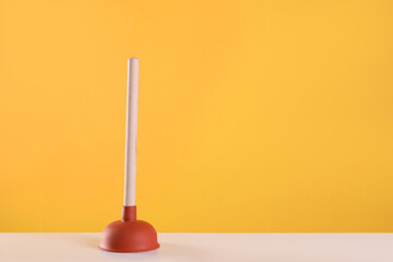 Plunger on white table against yellow background. Space for text