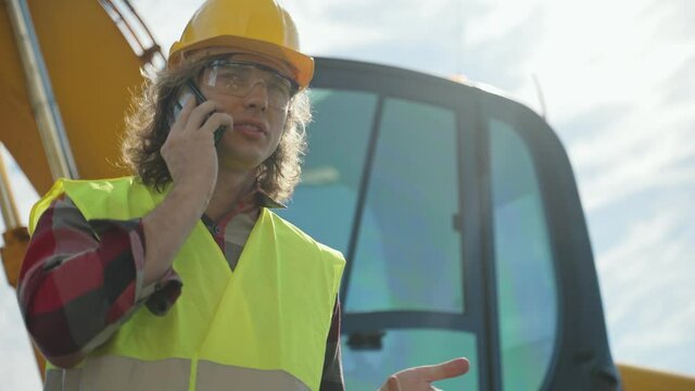 Excavator operator in hard hat talking by smartphone.
