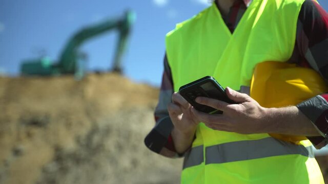 Builder with hard hat and high vis jacket using smartphone. Close-up.