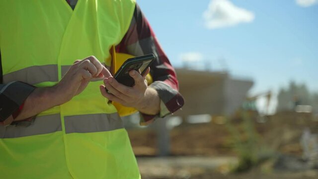 Builder with hard hat and high vis jacket using smartphone. Close-up.