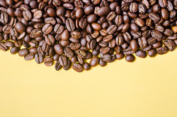 Roasted coffee beans on yellow background with copy space.