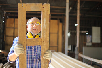 Senior Asian carpenter man is repairing wooden frame in his own garage style workshop at retirement age for hobby