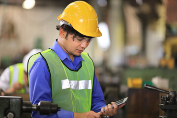 Asian engineering manager in safety hard hat and reflective cloth is inspecting inside the factory using digital tablet