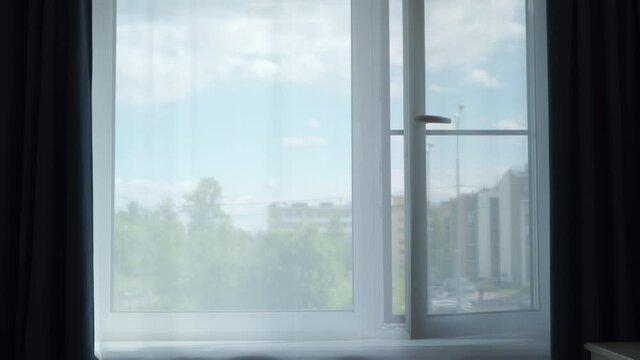 Transparent curtain on open window moved by the wind at sunny day, sun rays shine through the transparent tulle on window of apartment room. High quality 4k footage
