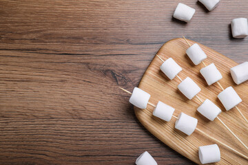 Sticks with delicious puffy marshmallows on wooden table, flat lay. Space for text