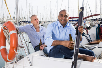 Two young men in blue shirts have a nice time on a private sailing yacht in the seaport