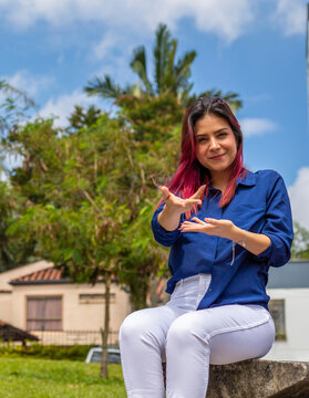 young woman sitting in outdoors making welcome gesture with her hands.