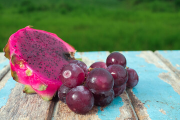 Red grapes and dragon fruit on wooden table with green field background , fresh fruit concept