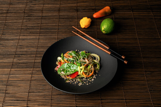 Vegan Vegetarisches Asia Gericht aus zucchininudeln und Gem&uuml;se mit St&auml;bchen auf Holzuntergrund 
