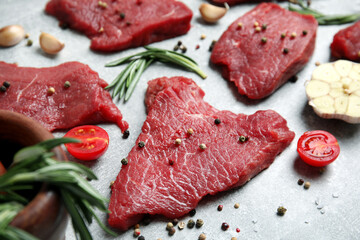 Fresh raw meat steaks and spices on light grey table, closeup