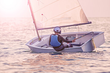 Handsome young boy learning to sail a sailing boat at sunset in the ocean
