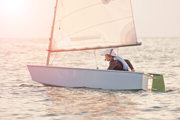 Handsome young boy learning to sail a sailing boat at sunset in the ocean