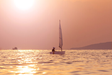 Fototapeta na wymiar Handsome young boy learning to sail a sailing boat at sunset in the ocean