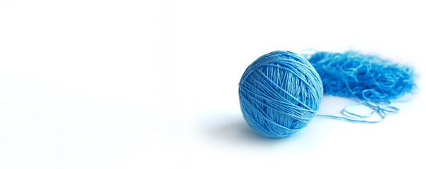 A ball of bright blue fine cotton yarn in the process of winding, isolated on the white background. Tangled yarn in the background. Long banner with space for text on the left.
