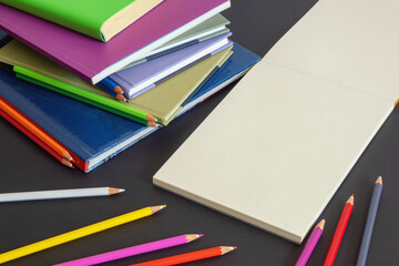 School concept. Stack of books, colorful colored pencils and open sketchbook on dark paper...