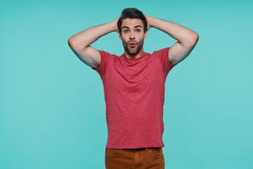 Fototapeta premium Excited young man in casual clothing looking at camera and holding hands on head
