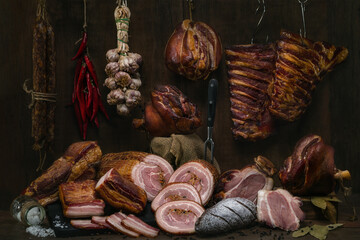 Smoked pork sausage, back ribs, pork neck, breast and knuckle. Traditional various smoked meats, vegetales and rye bread on a wooden table with background