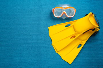 Pair of yellow flippers and mask on blue fabric, flat lay. Space for text © New Africa