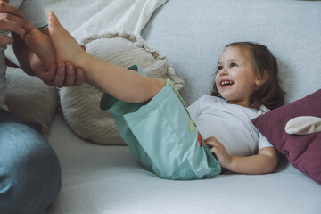 Father plays with little daughter 2-4 on couch. Dad tickles kids feet. Family, having fun