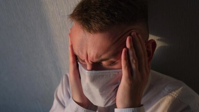 Man winces from headache as a symptom of covid-19