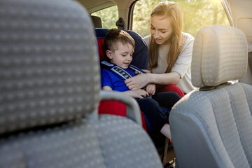 Protection in the car. Hands of caucasian woman is fastening security belt to child, who is sitting in safety car seat or chair. Toddler has a trip in summer day. Vehicle and transportation concept