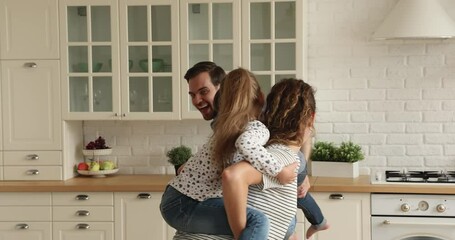 Happy joyful young couple parents giving piggyback ride to laughing sincere small son and daughter, involved in funny entertaining domestic active game in modern kitchen, having fun playing indoors.