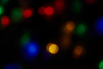 Defocused large bokeh multicolored lights on black background. Blurred abstract blue, green, red, orange spots. Blur bokeh spots wallpaper for Christmas, holiday background.
