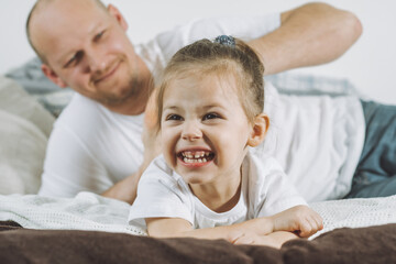 Father plays with little daughter 2-4 on bed. Dad tickles kids feet. Family, having fun