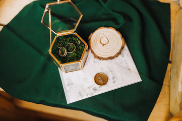 Close-up of the bride's wedding accessories: gold rings, a glass box with a rim, an envelope with a seal, an invitation.