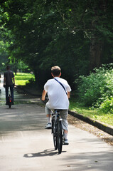 Obraz premium Sports activities in the park. A man rides a bicycle along the park alley. Healthy lifestyle.
