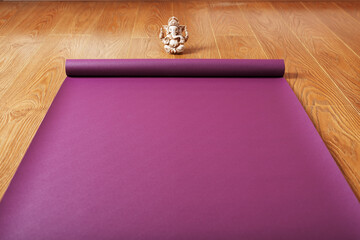 A lilac-colored yoga mat is spread out on the wooden floor with a Ganapati figurine