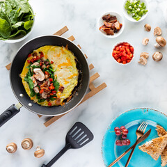 Top down view of ingredients used to make a breakfast omelette with the omelette being made in the frypan.