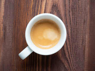 Close-up of a fragrant coffee in a white cup on a textured wooden background. Brown foam, top view, flat lay