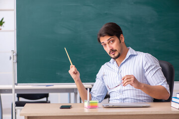Young male teacher in front of blackboard