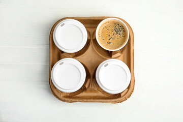 Takeaway paper coffee cups in cardboard holder on white wooden table, top view
