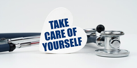 On a white background lies a stethoscope and a heart plate with the inscription - take care of...