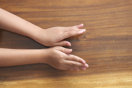 Two hands facing downwards, showing back of hand. Palm down, dorsal view, seen V letter. Wooden table texture as a background.