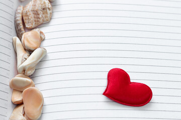 One woven bright red hearts lying on the page of an open diary or glider in a line with seashells...
