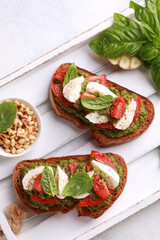 Italian cuisine. Rustic. Bruschetta with pesto sauce, fresh tomatoes, mozzarella and basil on a wooden board on a white table with pine nuts in bowl. Background image, copy space. Top view
