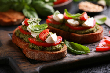 Italian cuisine. Rustic. Bruschetta with pesto sauce, fresh tomatoes, mozzarella and basil on a wooden board on a black table. Background image, copy space.