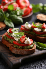 Italian cuisine. Rustic. Bruschetta with pesto sauce, fresh tomatoes, mozzarella and basil on a wooden board on a black table. Background image, copy space.