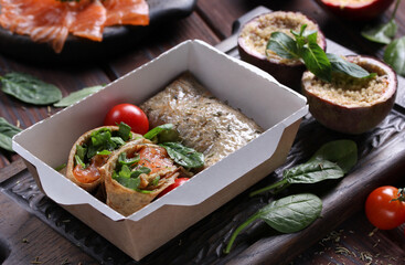 Food for delivery. Pancakes with with salmon, spinach and passion fruit dessert in a box on a gray wooden table. Rustic. Background image, copy space