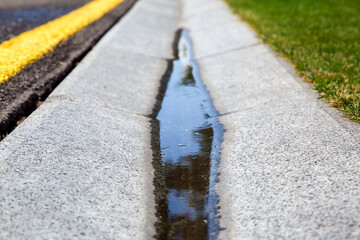 flowing rainwater in the canal is a cement ditch of a drainage system on the side of wet asphalt...