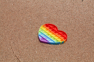 colorful antistress sensory pop it toy in form of heart on sand with water on beach. summer and relax concept. autism needs silicone stress relief toy